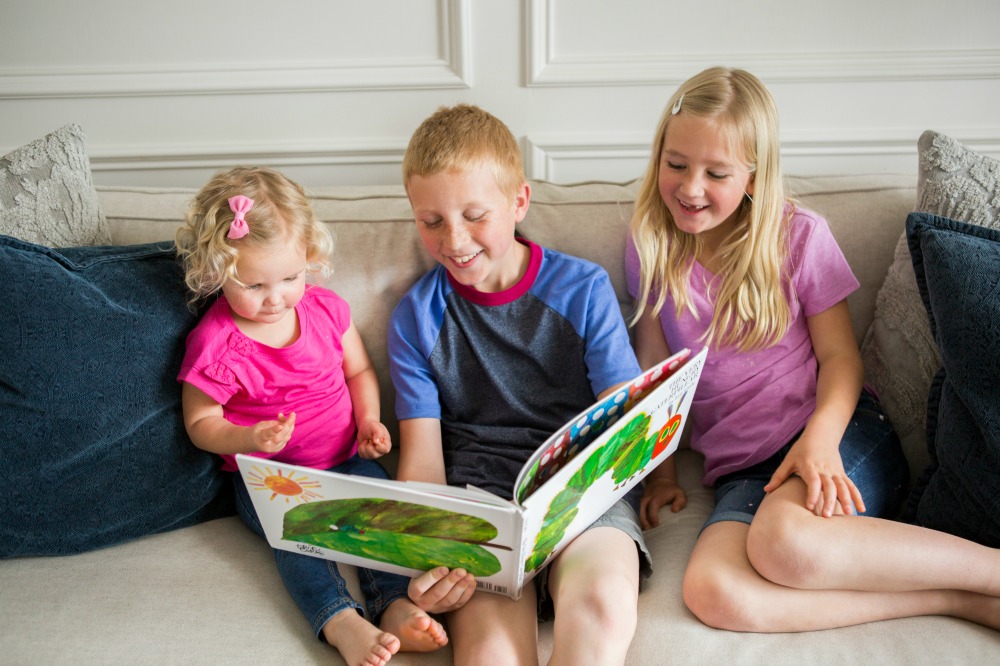 Siblings reading book on sofa for Virtual Book Club Summer Camp