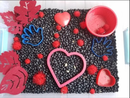 The Kissing Hand Sensory Bin with hearts and hand themed items.